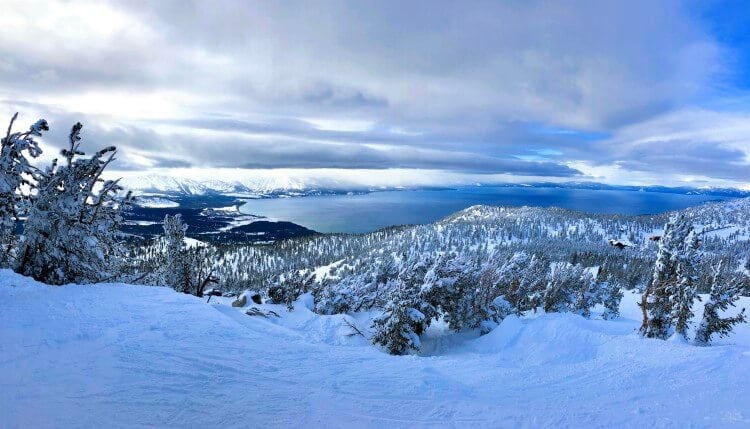 A snowy panorama of Lake Tahoe from a mountaintop looking down on the lake and forest