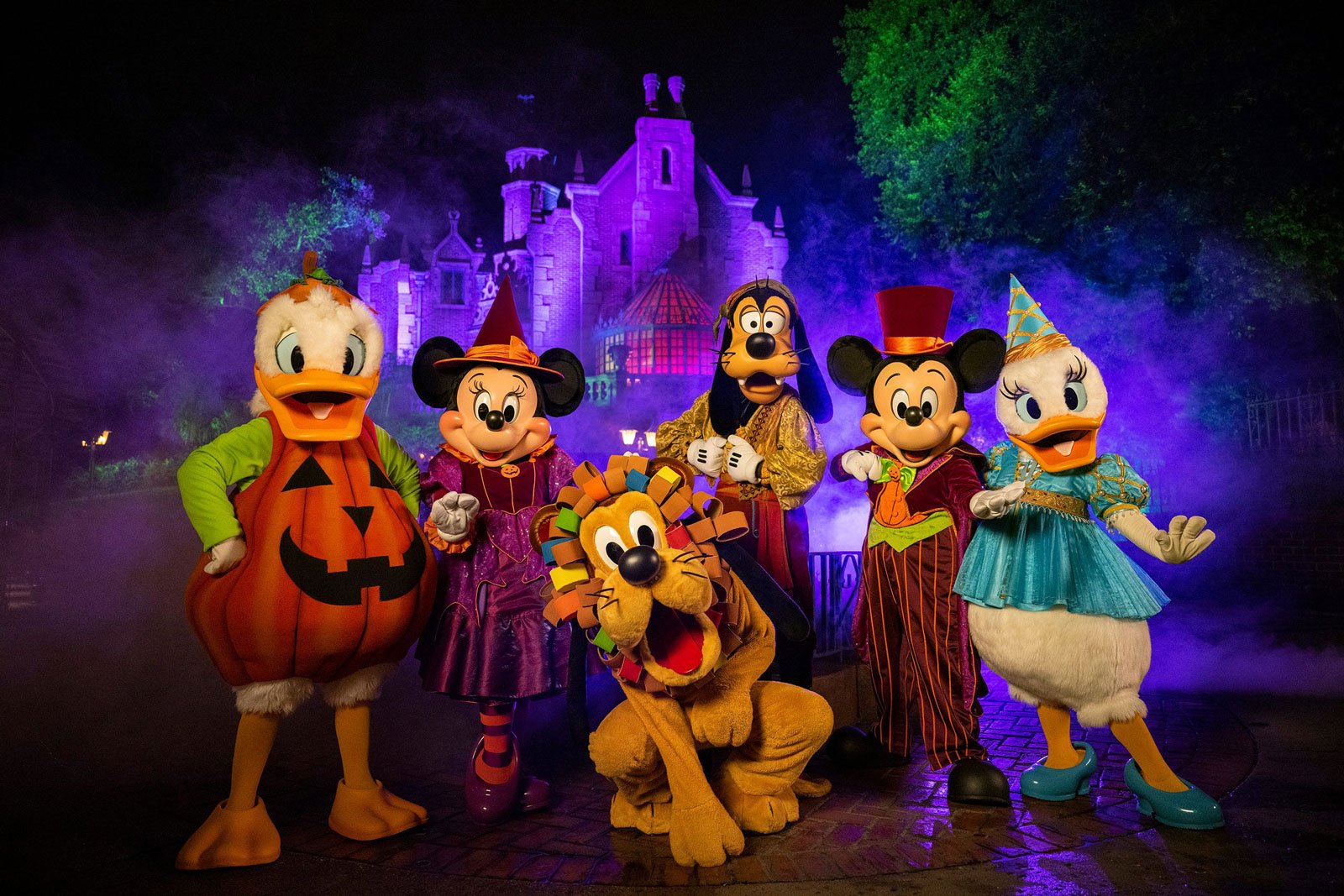Costumed performaers dressed as Mickey and Minnie Mouse, Pluto, Goofy, and Donald and Daisy Duck in front of Cinderella's Castle at the Disney World Halloween event