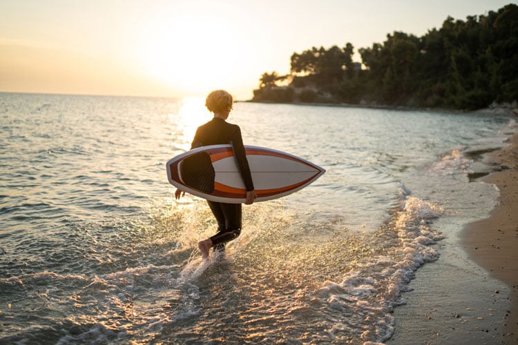 A person carrying a surfboard along a beach in Cabo - The best places to visit in August