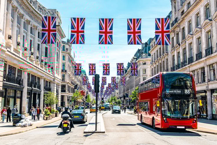 Red double decker bus in a wide street with Union Jack flags in London - The best places to visit in August