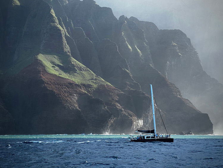 A sailboat in front of forest-covered mountains along the coast of Hawaii
