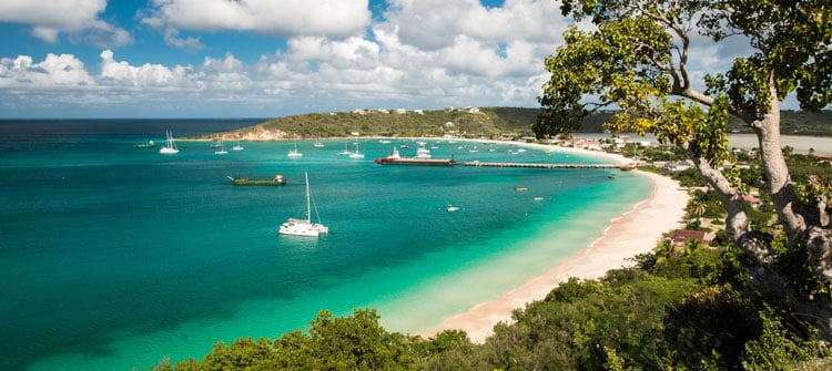 Sweeping white sand beach cove in Anguilla, with yachts and fishing boats in the water - a warm place to visit in January