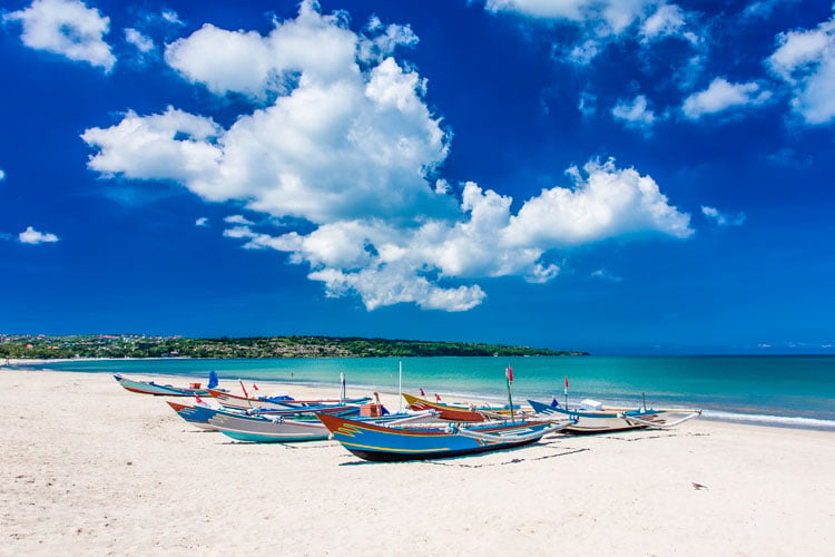 Fishing boast on a white sand beach in Bali with fluffy white clouds in the sky - one of the best beaches in January