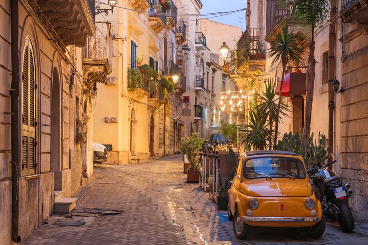 A cobbled street at twilight with a yellow Fiat 500 parked in Sicily - best places to visit in March