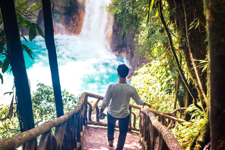 A man standing on wooden steps admiring a waterfall in Costa Rica - the best places to visit in May