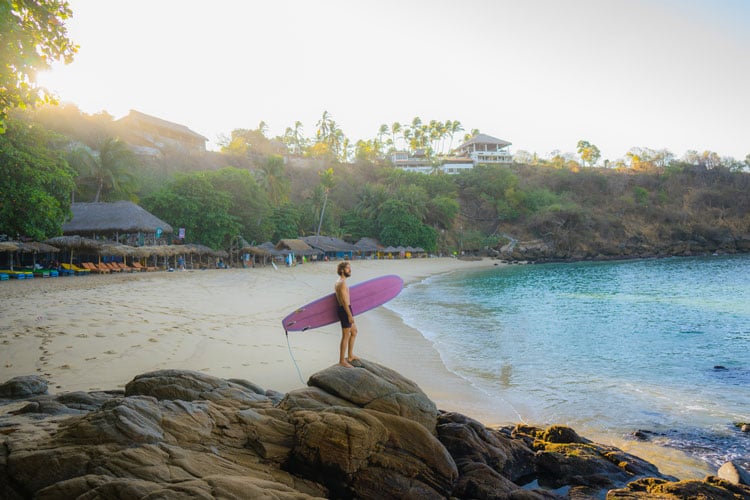The best places to visit in November - person carrying surfboard across white sand beach