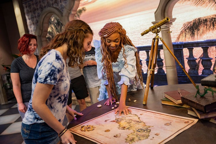 A young woman looking at a map with a lady playing Ariel from the Little Mermaid